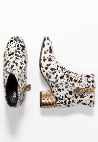 Kozaki za kostkę w gepardowy wzór z teksturowanej skórzanej cholewki, złotym, ćwiekowanym obcasem blokowym i zapięciem na zamek z boku. Kolor: czarno-biały.