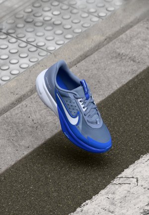 Zapatilla deportiva gris y azul con parte superior de malla, punta redondeada y logo Swoosh blanco. Los acentos texturizados y los cordones ofrecen un ajuste seguro.