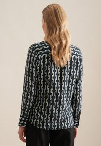 Camicia a maniche lunghe di colore verde scuro con un motivo a catena bianca. Presenta una trama liscia, polsini con bottoni e un orlo curvo.