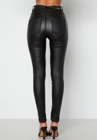 Svarta fusk läder skinny byxor med en slät yta, hög midja och två bakfickor. Combineras med svarta högklackade skor.