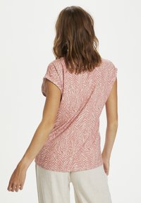 Růžový top s krátkým rukávem a texturovaným zebrovým vzorem, s uvolněným střihem a zavěšeným designem vzadu. Tkanina vypadá lehce a jemně.