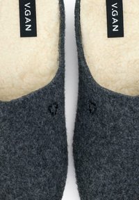 Gray felt slippers with a soft beige interior lining, featuring a rounded design and a small logo tag on the upper side.