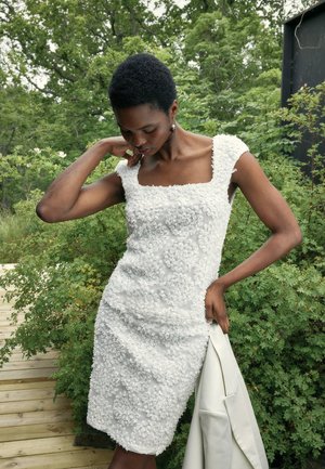 Robe blanche avec une texture florale, des pétales de tissu superposés, un décolleté carré, des manches courtes et une silhouette ajustée.