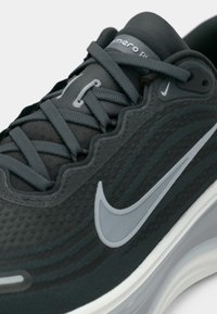 Σκούρο γκρι αθλητικό παπούτσι με υφή στην επάνω επιφάνεια, τονικά κορδόνια και λογότυπο swoosh σε ανοιχτό γκρι. Περιλαμβάνει μαλακή σόλα για υποστήριξη.