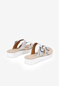 Sandalias de tiras cruzadas plateadas con material perforado, dos detalles de hebilla y una suela de plataforma blanca. Plantilla acolchada de color marrón claro.