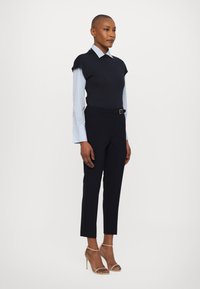 Marineblauwe top met korte mouwen over een lichtblauw gestreept shirt, gecombineerd met op maat gemaakte zwarte broek en nude sandaaltjes met bandjes.