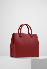 Röd läderhandväska med texturerad yta, som har två rundade handtag, en strukturerad form och dragkedjestängning.