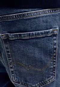 Zadné vrecko tmavomodrých riflí so žltým prešívaním a zakrivenými dekoratívnymi švami.