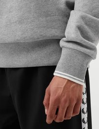 Felpa grigia con polsini e orlo a coste, con un accento di striscia bianca. Pantaloni neri con un motivo floreale ripetuto sui lati.