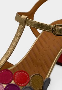 Sandale en cuir doré avec une bride texturée, ornée d'accents circulaires multicolores en rose, rouge, marron et gris, avec une semelle à motif.