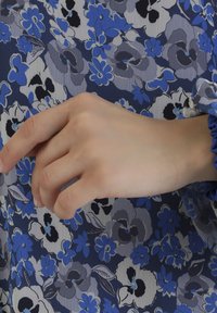 Tkanina w kwiatowy wzór w odcieniach niebieskiego, z granatowym tłem i szarymi oraz czarnymi akcentami. Dłoń dotyka materiału, ukazując jego fakturę.