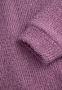 Fioletowa dzianina prążkowana o miękkiej fakturze i puszystym wykończeniu, z fałdem materiału, ukazującym głębię i ciepło.