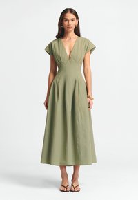 Alyvuogių žalios spalvos maksi suknelė su giliu V formos kaklu, trumpomis rankovėmis ir klostuota sijonu. Pagaminta iš minkštos medžiagos su lygiu paviršiumi.