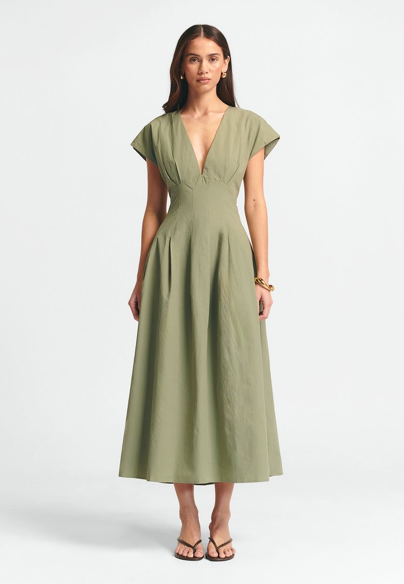 Alyvuogių žalios spalvos maksi suknelė su giliu V formos kaklu, trumpomis rankovėmis ir klostuota sijonu. Pagaminta iš minkštos medžiagos su lygiu paviršiumi.