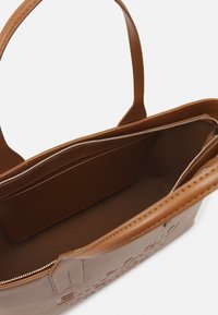 Braune Ledertasche mit geprägtem Design, einem Hauptfach und einer Reißverschlusstasche. Verfügt über stabile Griffe und eine glatte Textur.