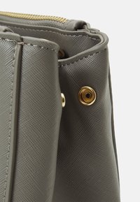 Szara teksturowana torebka syntetyczna z złotym zamkiem błyskawicznym i dekoracyjnym detalem metalowym. Boki są wzmocnione przeszyciami.