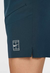 Marinblå sportshorts med en liten slits vid fållen, med en vit Nike-logotyp inom en rektangulär kontur på vänster sida.