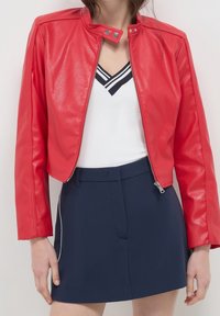 Rode faux leren jas met een cropped ontwerp, ritssluiting en drukknopenkraag. Gecombineerd met een wit topje en marineblauwe korte broek. Gladde textuur.