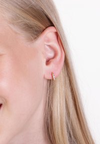 Gold hoop earring with small clear stones, featuring a textured surface and a smooth, curved design, worn on a person’s ear.