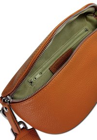 Bruine leren tas met een ronde vorm, voorzien van een groene stoffen binnenkant en een ritssluiting. Inclusief een klein binnenvak.