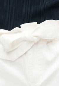 Λευκό παντελόνι με υφασμάτινη ζώνη δεμένη σε φιόγκο σε ελαστική μέση, συνδυασμένο με μαύρο ριμπ τοπ.