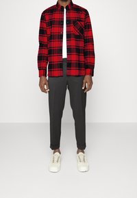 Camicia di flanella a scacchi rossi e neri, con bottoni, e tasca sul petto. Abbinata a pantaloni grigi a sigaretta e sneakers bianche.