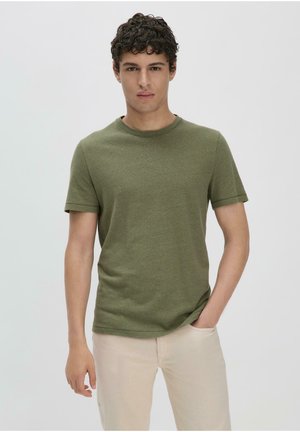 Olijfgroen t-shirt met korte mouwen, gemaakt van zacht katoen, met een ronde hals en een relaxte pasvorm. G gedragen met lichtgekleurde broeken.