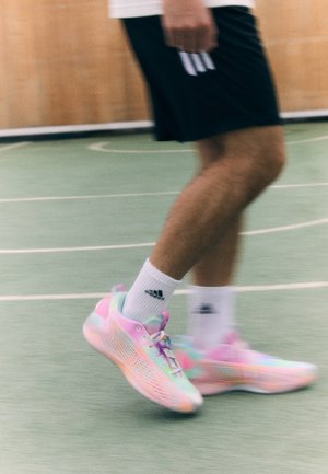 Osoba ubrana w czarne spodenki i białe skarpetki Adidas, chodząca po zielonym krytym boisku sportowym, nosząca pastelowe buty do biegania.