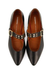 Zapatos Mary Jane de cuero negro con punta afilada, con una correa texturizada, tachuelas en tono dorado y un forro interior marrón.