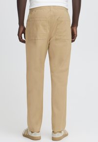 Beige cotton pants with an elastic waistband, featuring two large back pockets and a relaxed fit, paired with beige sneakers.