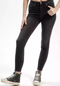 Czarne dżinsy skinny z wysokim stanem, zaprojektowane w tradycyjnym pięciokieszeniowym stylu z subtelnymi detalami przeszyć, w połączeniu z czarnymi wysokimi trampkami.