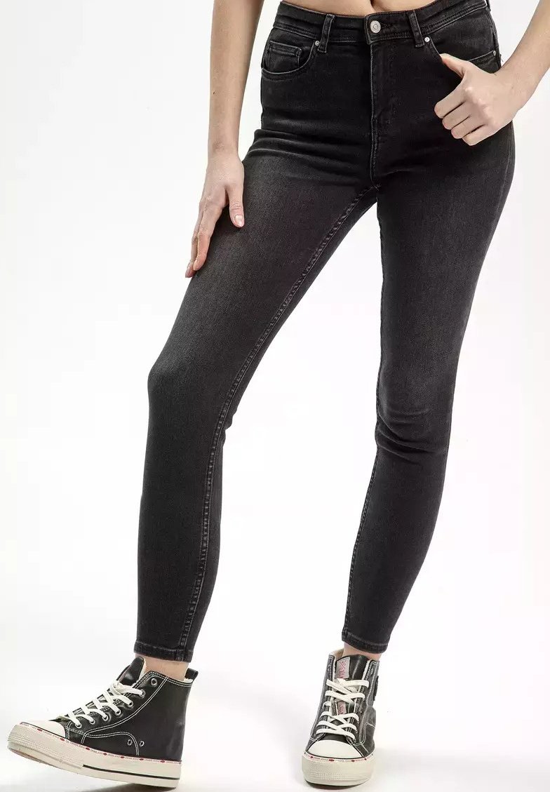 Czarne dżinsy skinny z wysokim stanem, zaprojektowane w tradycyjnym pięciokieszeniowym stylu z subtelnymi detalami przeszyć, w połączeniu z czarnymi wysokimi trampkami.