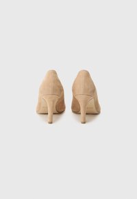 Chaussures à talons hauts en daim nude avec un bout pointu et un talon effilé. Texture lisse avec un design sans coutures, affichant un branding minimal visible.