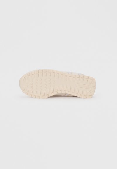 Semelle de sneaker beige avec une surface en caoutchouc texturé, présentant un motif de bande de roulement pour une adhérence et un renfort à l'avant pour une durabilité accrue.