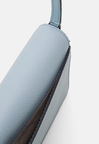 Borsa a tracolla in pelle texturizzata blu chiaro con una sottile tracolla, parzialmente aperta per mostrare l'interno foderato in tessuto scuro.