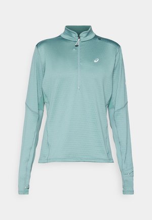 Langarm-Pullover in hellem Türkis mit einem halben Reißverschlusskragen, strukturiertem Stoff mit einem Wabenmuster und reflektierenden Akzenten an den Ärmeln.