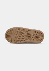 Suela de un zapato con una textura de goma color marrón claro, que presenta un dibujo de surcos para mayor tracción, y una zona central lisa con bordes definidos.