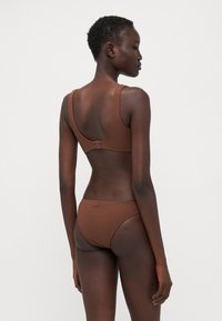 Brunt ribbet bikini sett med en teksturert finish. Toppen har brede stropper og en spennelukking, mens bunnen har et enkelt, lave skår.