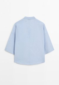 Chemise bleu clair oversize avec manches larges et ourlet droit, présentée à plat sur un fond blanc, vue de dos.