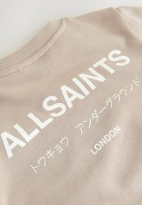 Beige katoenen sweatshirt met een ribgebreide halslijn, met opvallende witte tekst "ALLSAINTS" en aanvullende meertalige tekst eronder.