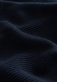 Dark navy fabric with a soft, ribbed knit texture, showing gentle folds and wave-like patterns.