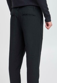 Schwarze Hosen aus glattem Stoff, mit einer taillierten Passform, seitlichen Taschen und zwei Gesäßtaschen mit schmalen Öffnungen.