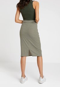 Proužkovaná tužková sukně v černé a béžové barvě s rozparkem na zádech, doplněná o úzký zelený top a bílé tenisky.