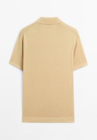 Polo a maniche corte in cotone beige chiaro, con colletto classico e orlo a coste. Tessuto liscio senza motivi visibili.