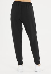 Zwarte trainingsbroek met een elastische tailleband, taps toelopend ontwerp en een gladde textuur, gecombineerd met witte sportschoenen.
