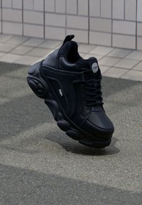 Black leather sneaker with chunky sole, rounded shape, and textured accents. Features lace-up front and logo detail on side.