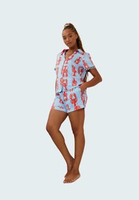 Conjunto de pijama con patrón de langostas en azul claro, que incluye una camiseta de botones de manga corta y pantalones cortos a juego con detalles de rayas en blanco y negro.