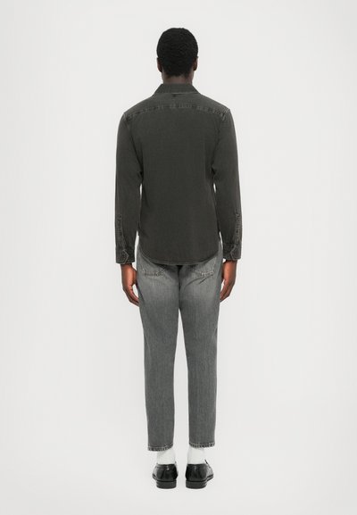 Dunkelgraues Langarmhemd mit Kragen, Knopfmanschetten und leicht abgerundetem Saum, getragen mit hellgrauen geraden Jeans und schwarzen Schuhen.
