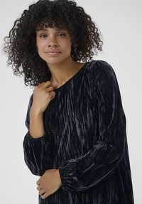 Rochie din catifea neagră cu textură în dungi verticale, decolteu rotund și mâneci lungi, burtite. Țesătura pare moale și luxoasă.
