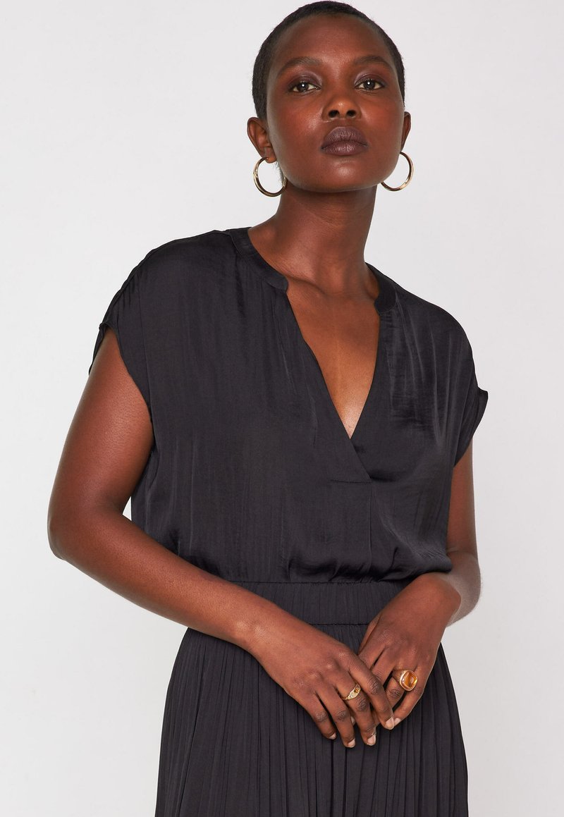 Blusa nera in seta con scollatura a V, maniche corte e vestibilità morbida. Il tessuto ha una texture liscia, cade delicatamente ed è caratterizzato da una leggera lucentezza.